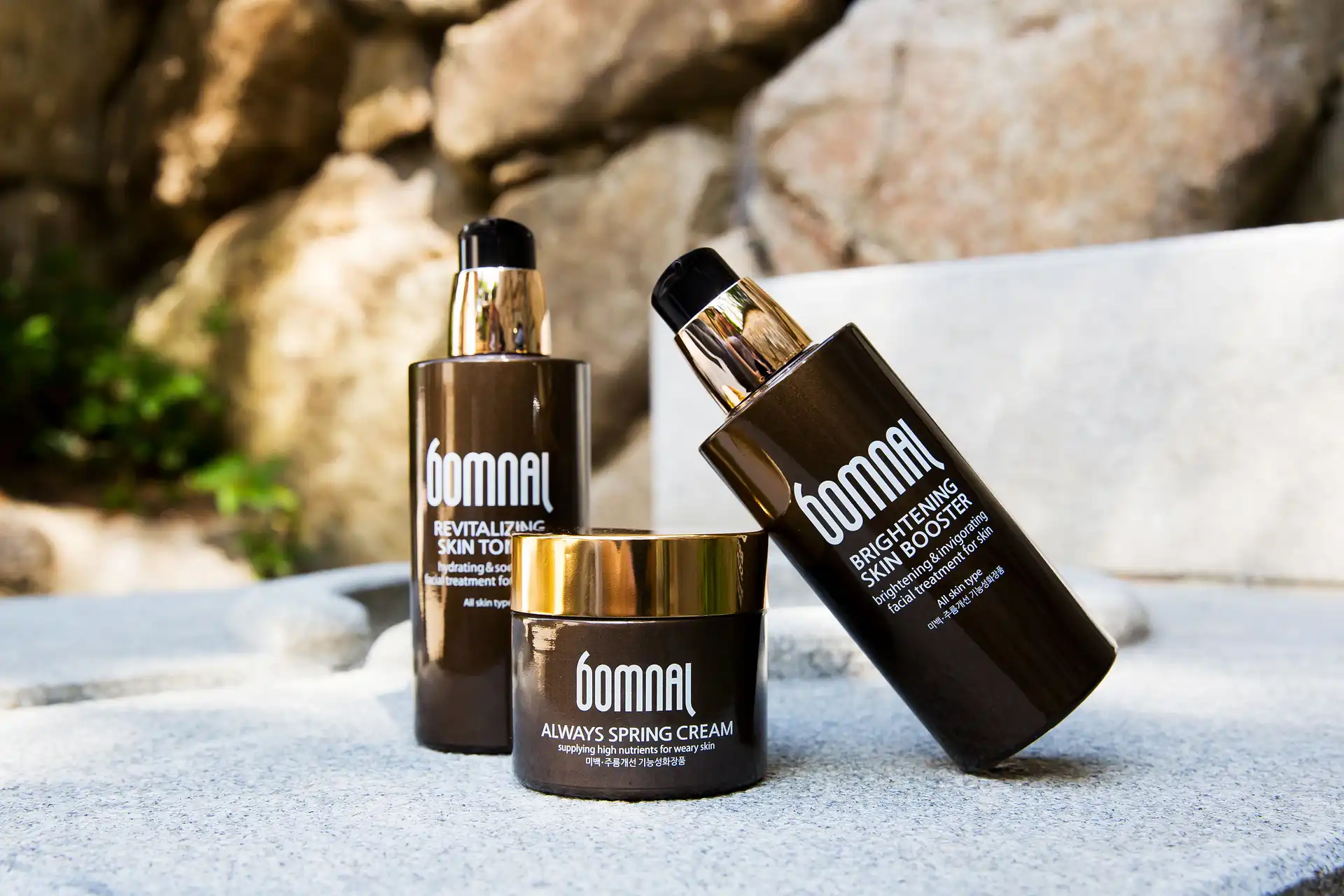 Skincare bottles and a jar styled on a sunlit stone surface